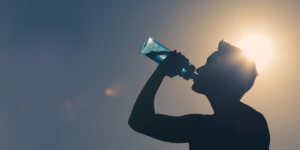 A silhouette of a man drinking a bottle of water as the sun beams behind him.