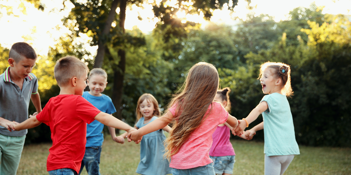 A group of kids playing ring around the rosie together outside in the summer
